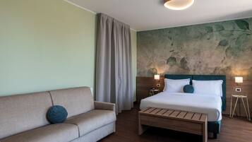 A hotel room with a bed, a sofa, a bedside table, and a wall with a leaf pattern.