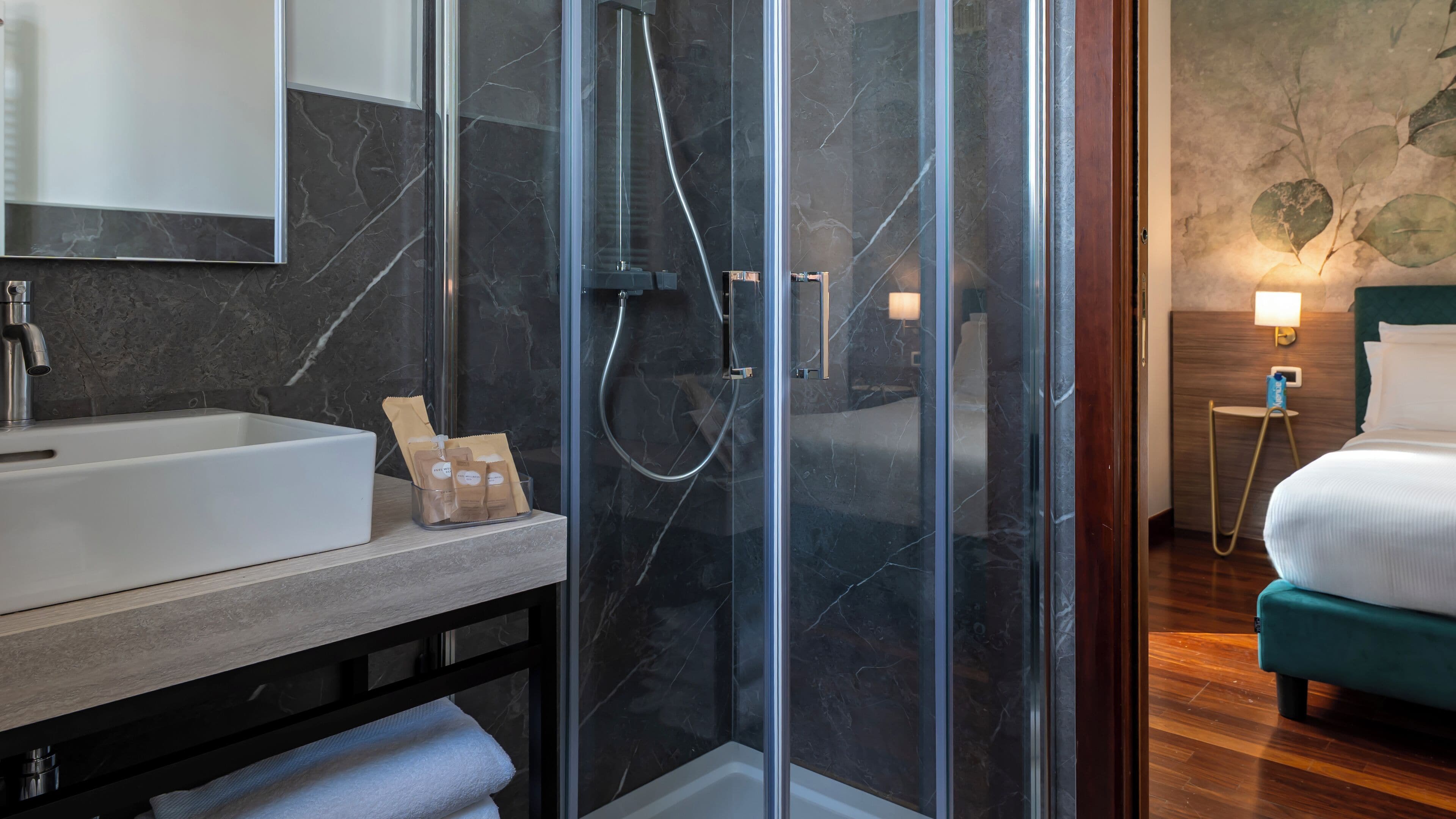 Un baño moderno con ducha envuelta en vidrio, un lavamanos blanco y pared con azulejos de mármol.
