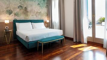 A modern hotel room with a teal bed, wooden flooring, and a view of the city through large windows.