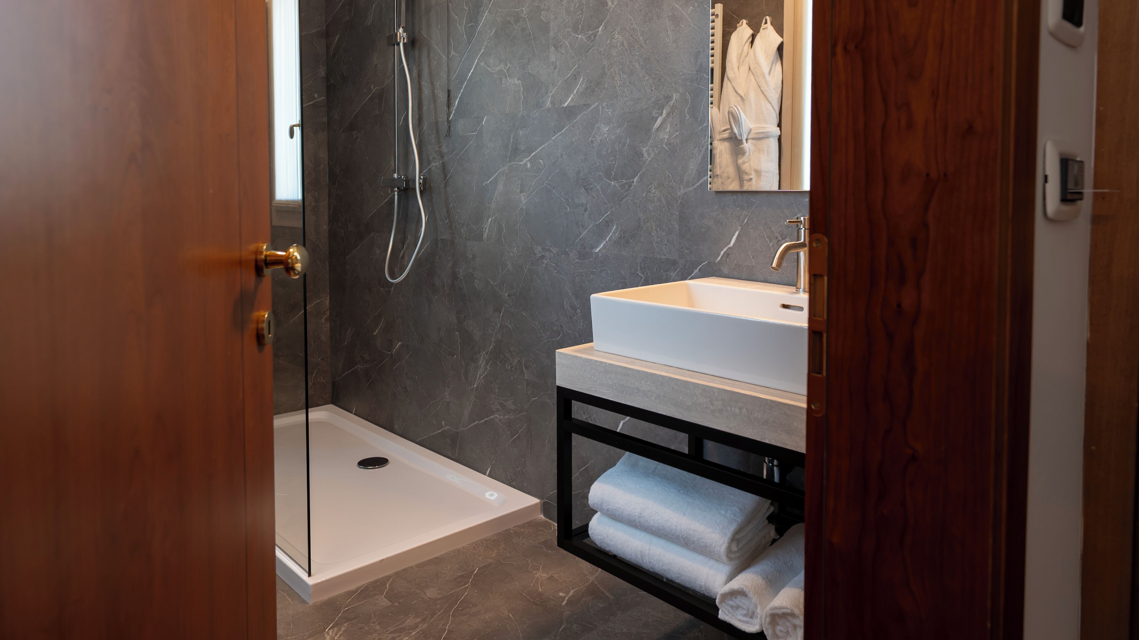 A modern bathroom with a glass-enclosed shower, a white sink, and a marble-tiled wall.