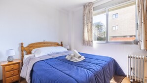 Ein Schlafzimmer mit einem hölzernen Bett, einem Nachttisch mit Lampe und einem Fenster mit Vorhängen.