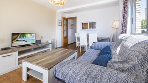 Ein Wohnzimmer mit Fernseher, Couch, Holztisch und einem Essbereich mit Tisch und Stühlen.