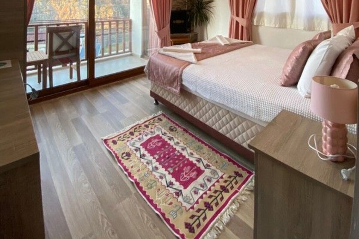 A bedroom with a large bed, a balcony with a view, and a wooden floor.