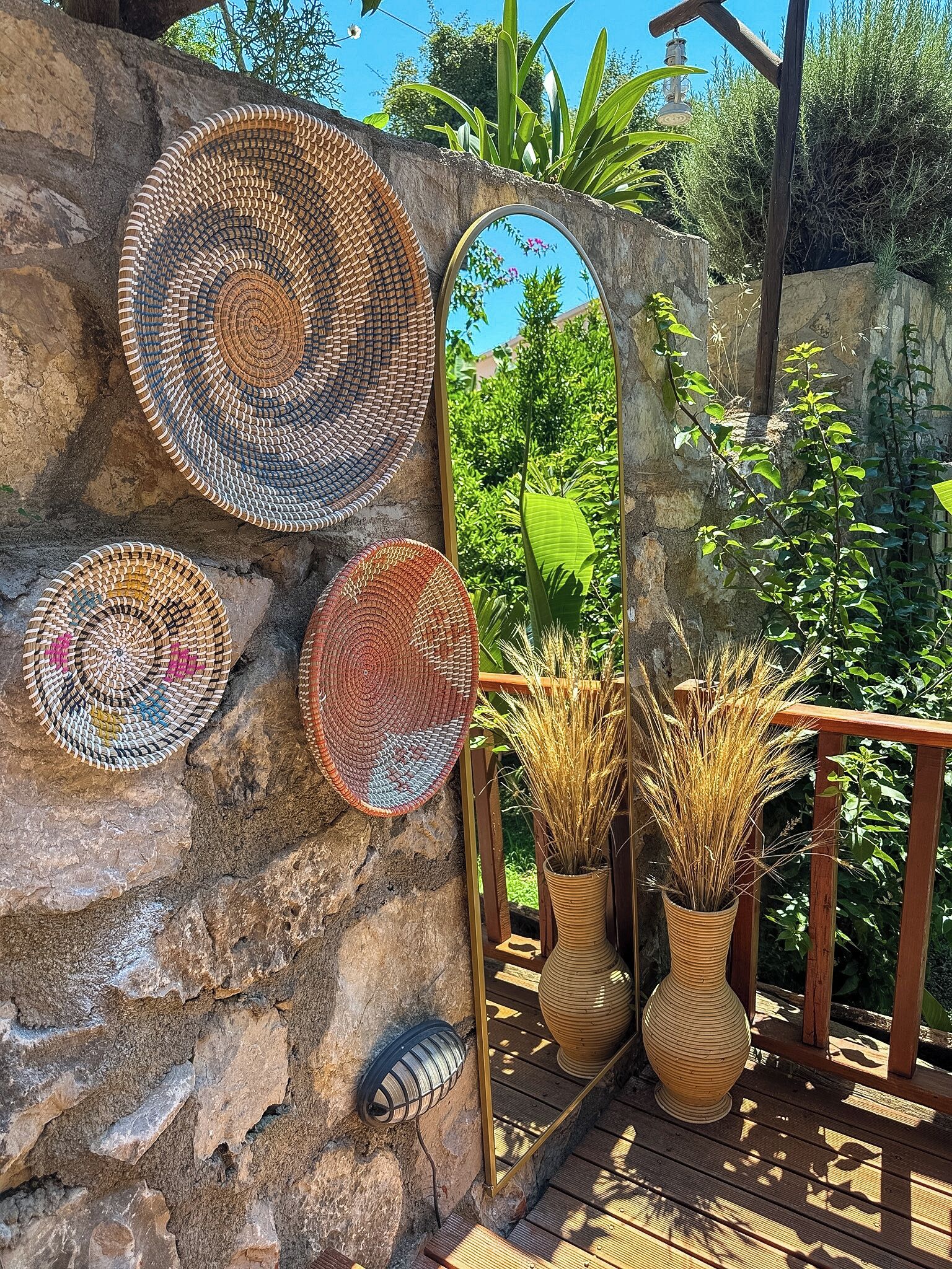 Woven baskets on a stone wall, a wooden railing, and two potted plants.