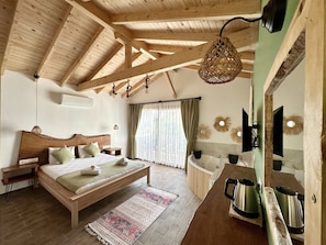 A wooden-framed bedroom with a bed, bedside tables, a hanging light fixture, a large mirror, and a bathroom with a bathtub and a sink. - Faralya Misafir Evi (Fethiye)