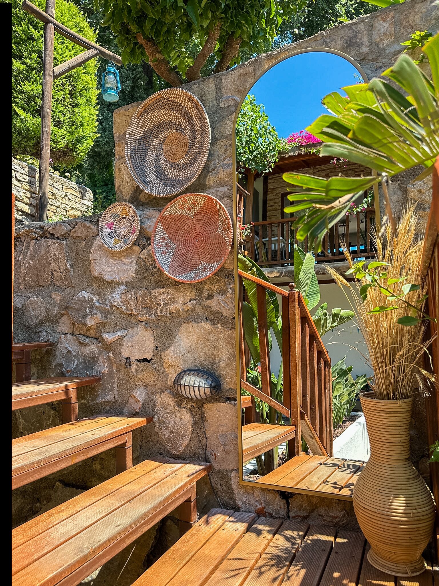 Un muro de piedra con cestas tejidas, bancos de madera y una planta en maceta.