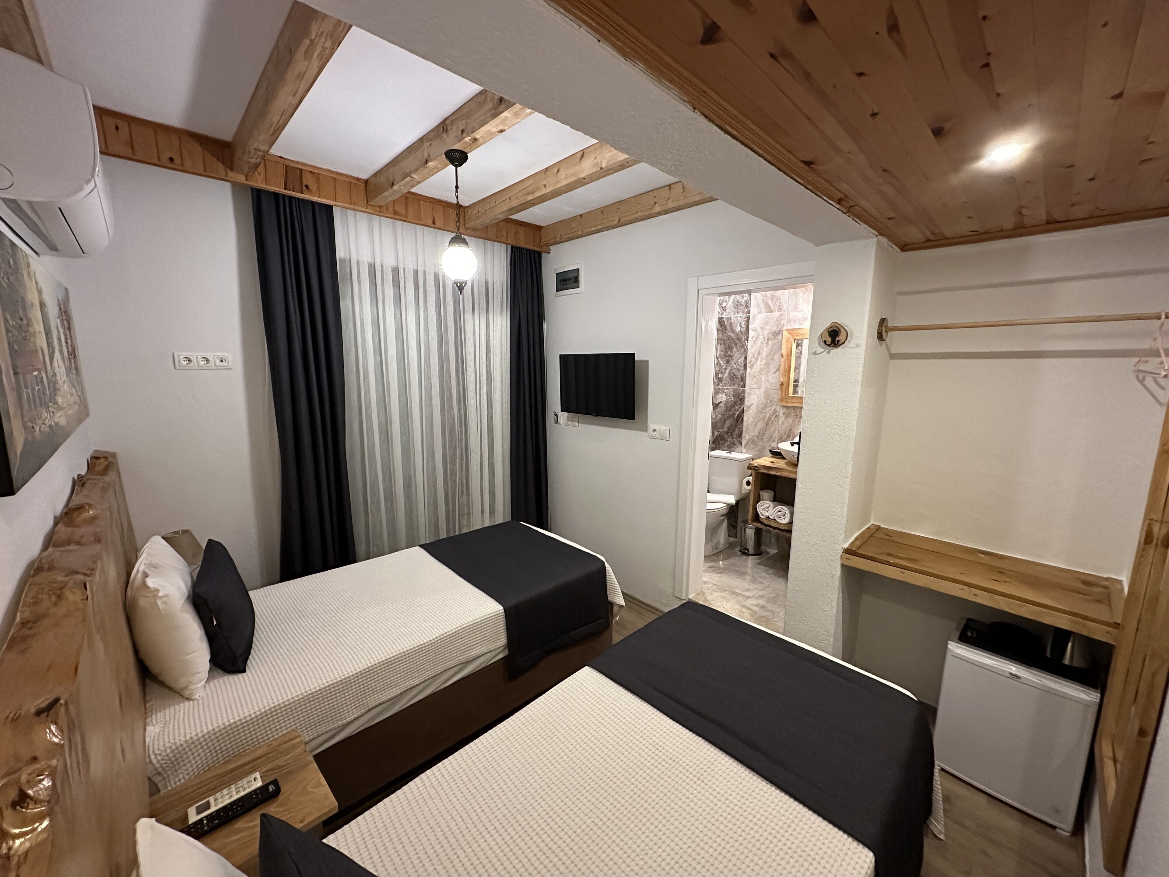Un dormitorio con dos camas, vigas de madera en el techo, un televisor y una pequeña kitchenette.