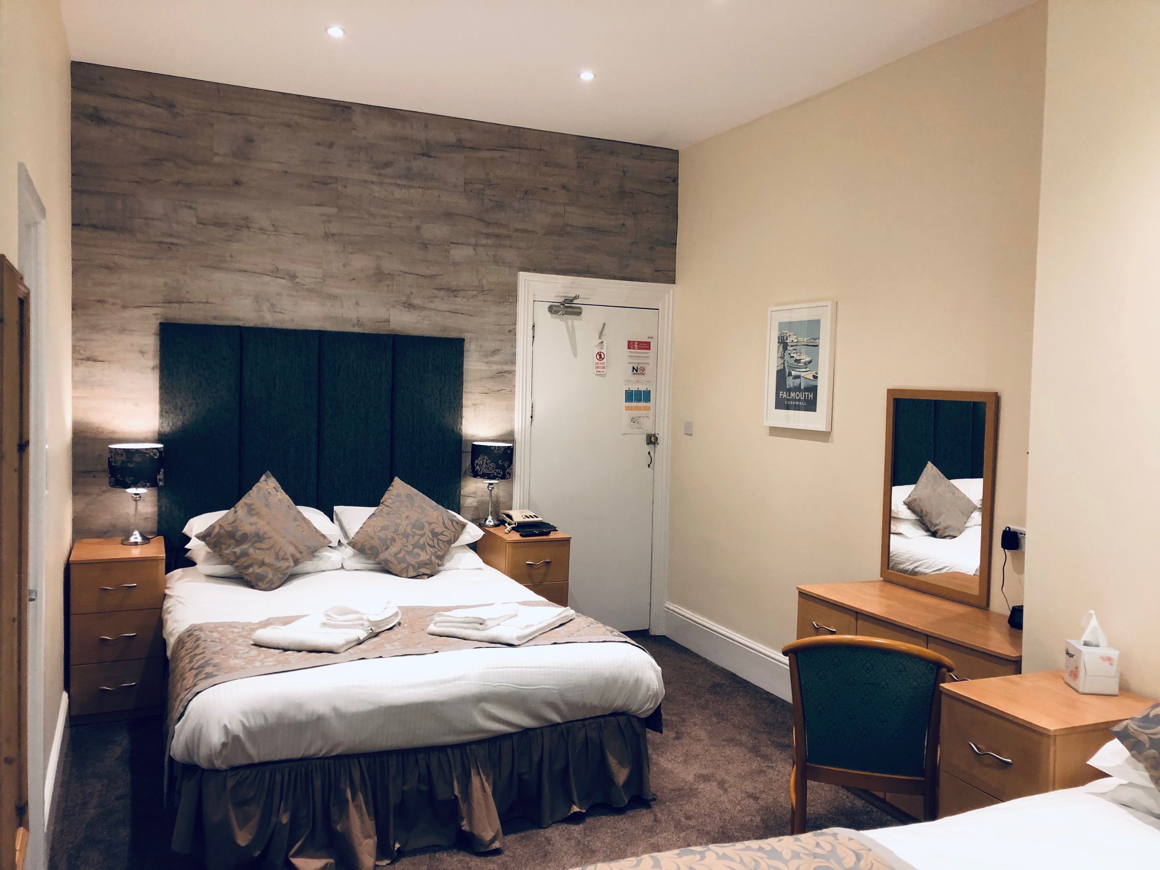 Ein Hotelzimmer mit einem großen Bett, Nachttischen, einem Schreibtisch und einem Spiegel.