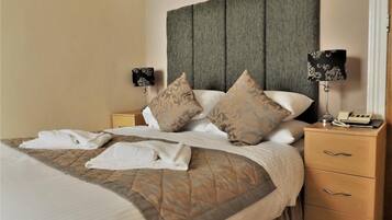 A neatly made bed with a patterned bedspread, two bedside lamps, a telephone, and a wooden nightstand with drawers.