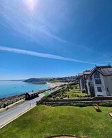 Una propiedad costera con un camino que lleva a un edificio blanco de grandes ventanales, con vista a una playa y al mar.