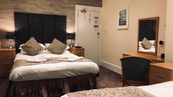 Habitación de hotel con una cama grande, una mesita de noche, un escritorio, una silla, un espejo y una puerta.