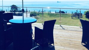 Um terraço ao ar livre com mesas e cadeiras sob grandes guarda-sóis, com vista para a praia e o oceano.