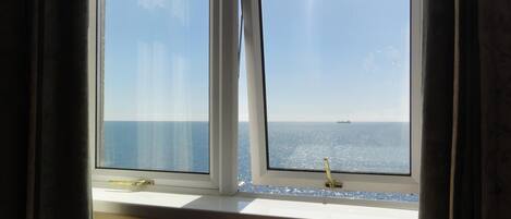A window with a view of the sea and a ship in the distance.