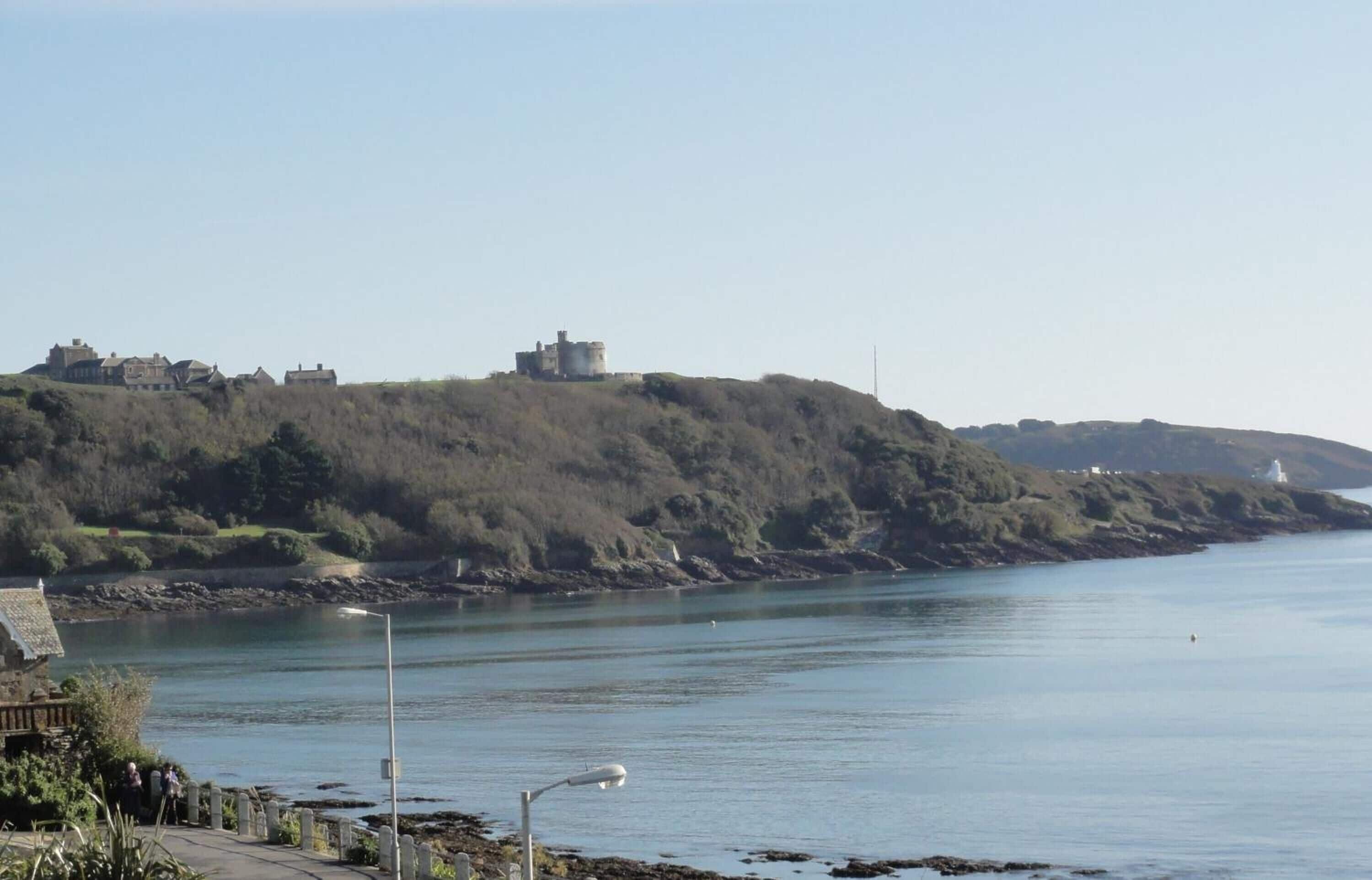 Paesaggio costiero con una collina che presenta una struttura simile a un castello, un faro e un mare calmo.