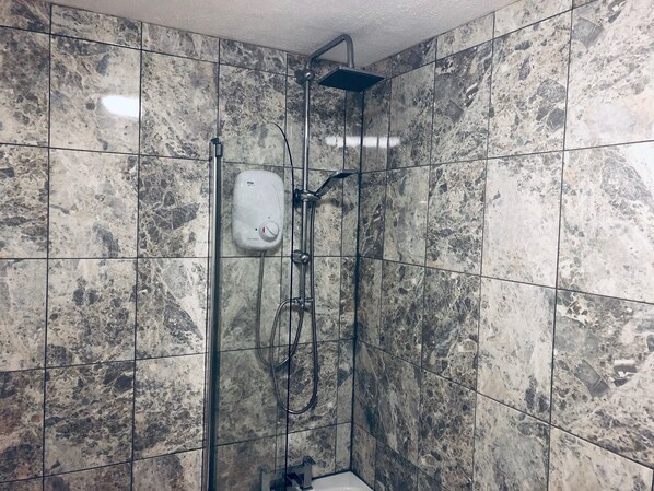 A shower area with a handheld showerhead, a wall-mounted control panel, and a tiled floor. - Membly Hall Hotel (Falmouth)