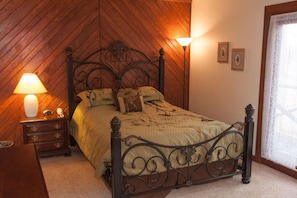 Un dormitorio con cama, mesita de noche, lámpara y ventana con cortinas de encaje.