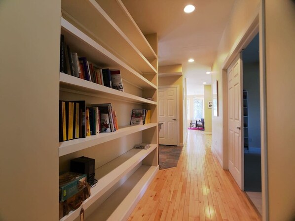 A hallway with wooden flooring and white shelving units containing books and decorative items.