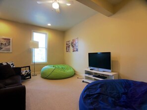 A room with a television on a stand, a bean bag chair, a couch, and a floor lamp.