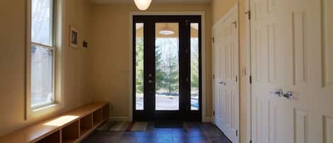 Un couloir avec un banc, une porte donnant sur une vue agréable et un luminaire au plafond.