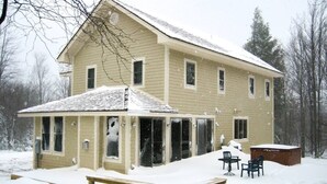 Ein zweistöckiges Haus mit einer überdachten Veranda, einer Holzterrasse und einem Whirlpool.
