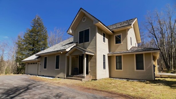 Ein zweigeschossiges Haus mit Veranda, Garage und Auffahrt.