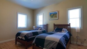Ein Schlafzimmer mit zwei Holzbetten, einem Deckenventilator und zwei Fenstern mit Jalousien.