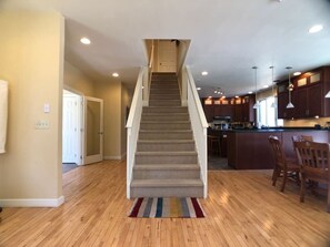 A staircase leading to a second floor, a kitchen area with wooden cabinets, and a dining area with chairs.
