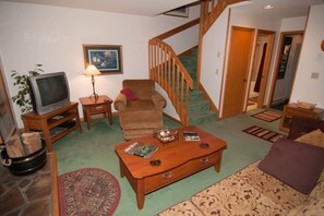 Un salon comprenant un téléviseur, un canapé, une table basse, un escalier et une porte donnant sur une autre pièce.