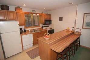 Une cuisine avec des meubles de rangement en bois, un four à micro-ondes, un réfrigérateur, un évier et un plan de travail en bois.