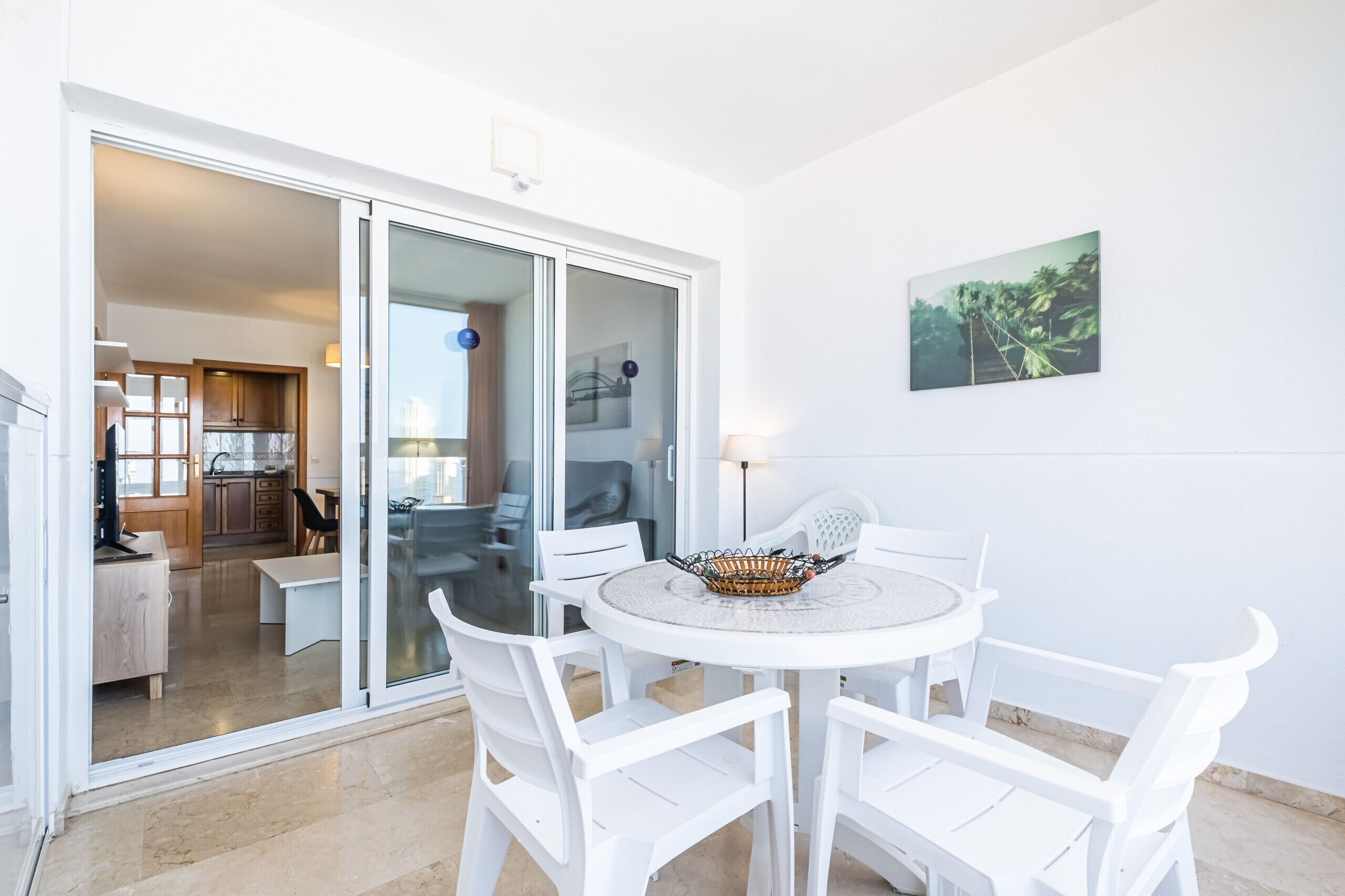 A modern room with a round table and white chairs, a glass door leading to a kitchen, and a framed picture on the wall.