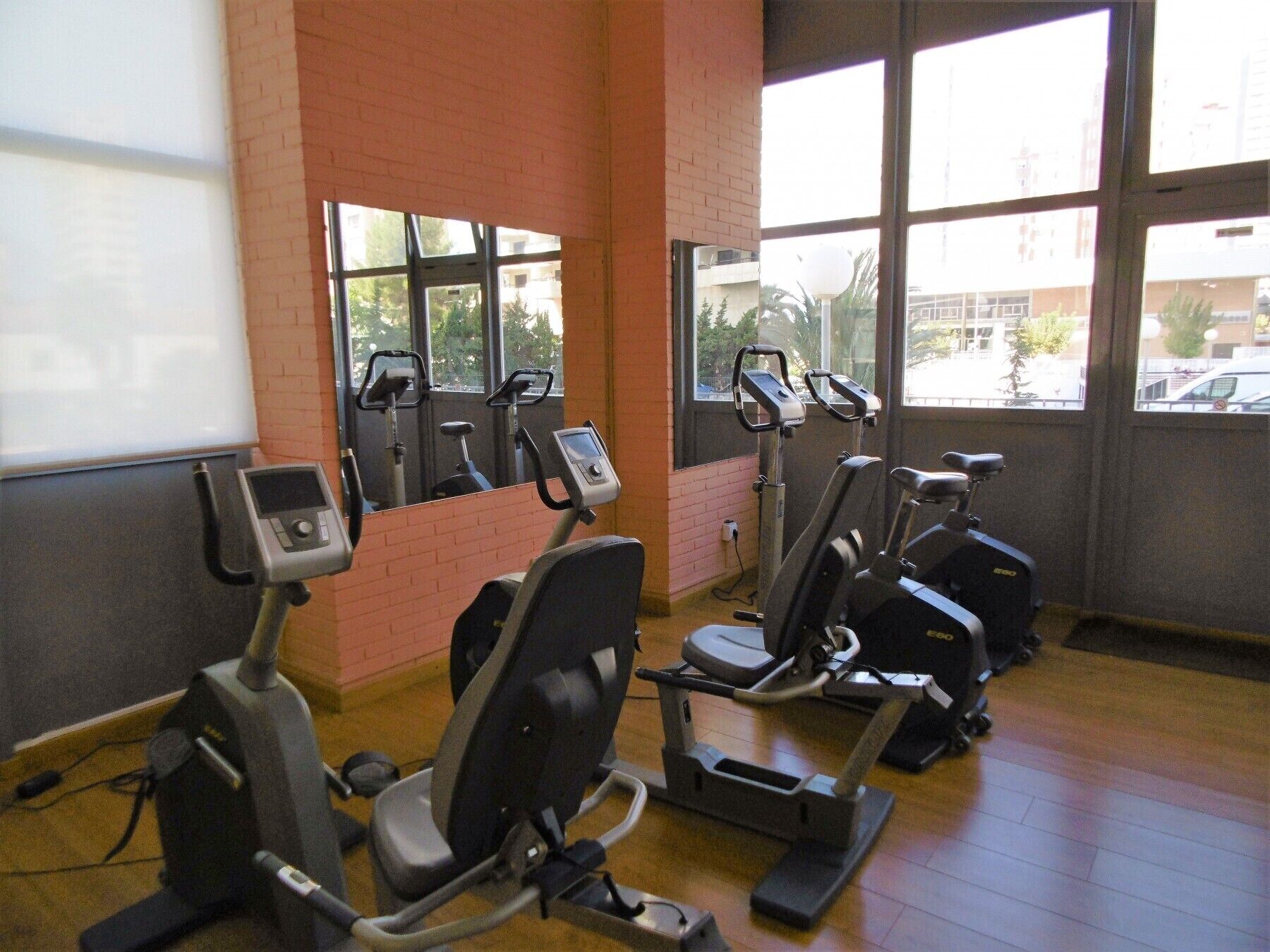 Et fitnesscenter med træningsudstyr, store vinduer og en murstensvæg.