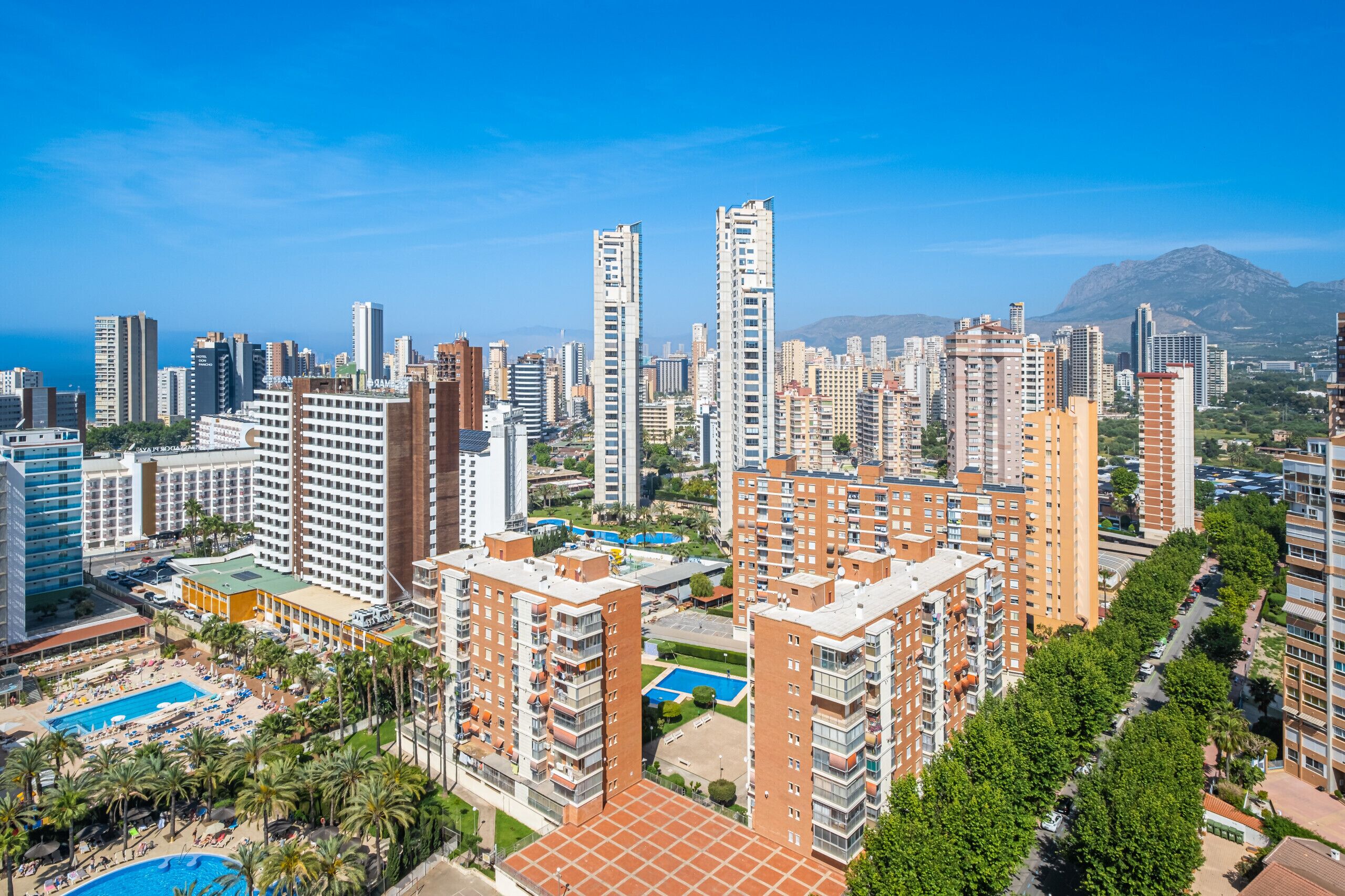 A high-rise hotel complex with multiple buildings, a swimming pool, and a view of the city and mountains in the background.