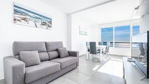 A modern living room with a grey sofa, a flat-screen TV, and a dining area with a table and chairs.