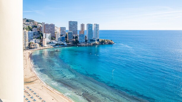 A coastal cityscape with high-rise buildings, a beach, and clear blue waters.