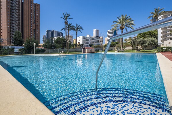 A swimming pool with clear blue water, surrounded by a tiled deck and palm trees. - Lidersol 11-D (Benidorm)
