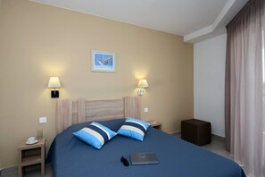Una habitació d'hotel amb un llit, dues làmpades de nit, un quadre amb marc a la paret, un ordinador portàtil al llit i un petit tamboret de fusta.