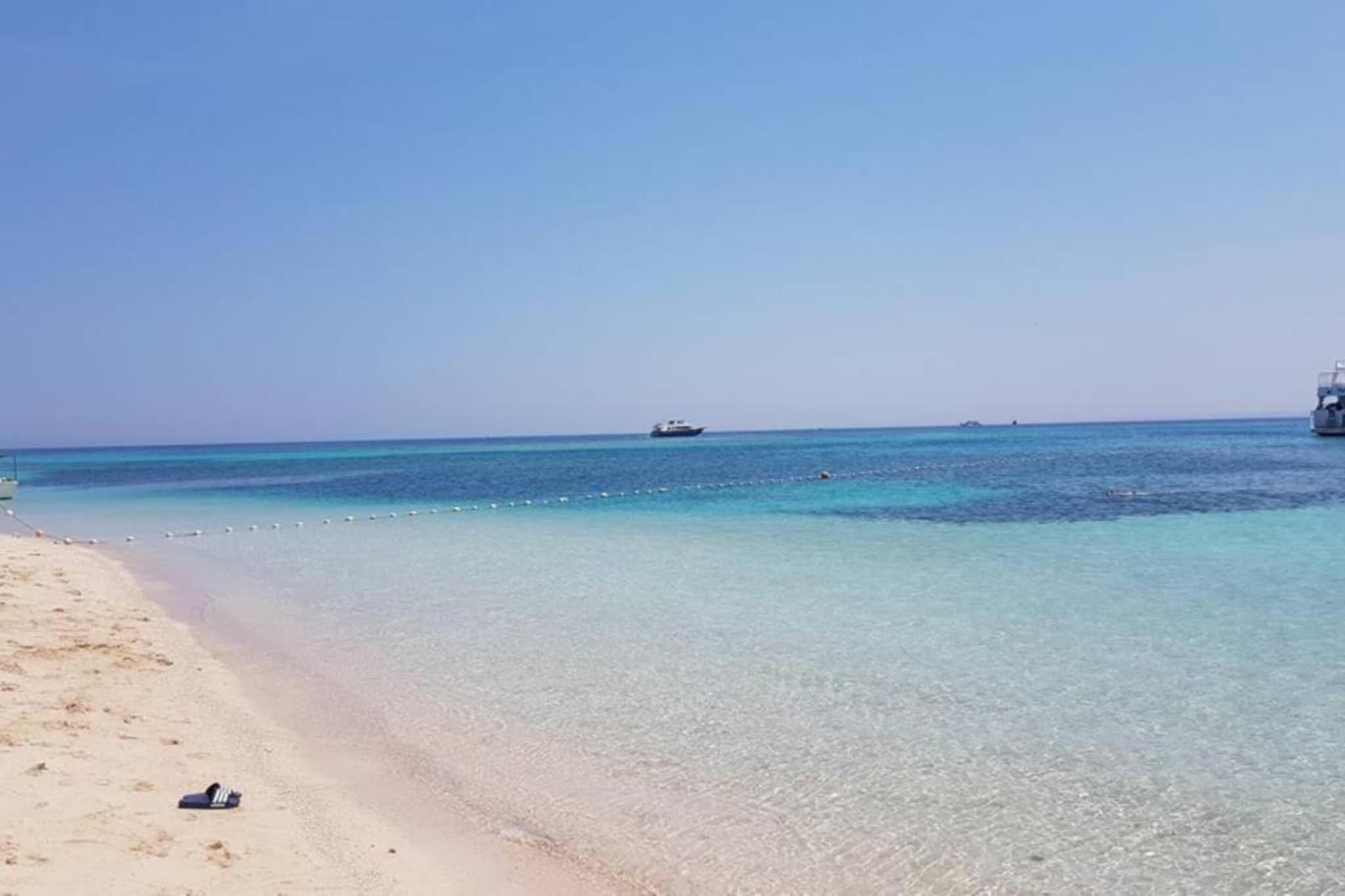 A beach with clear turquoise water, a boat in the distance, and a sandy shore.