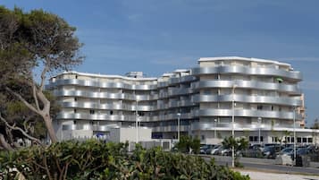 Un edificio residencial de varios pisos con balcones, zona de estacionamiento y vegetación circundante.