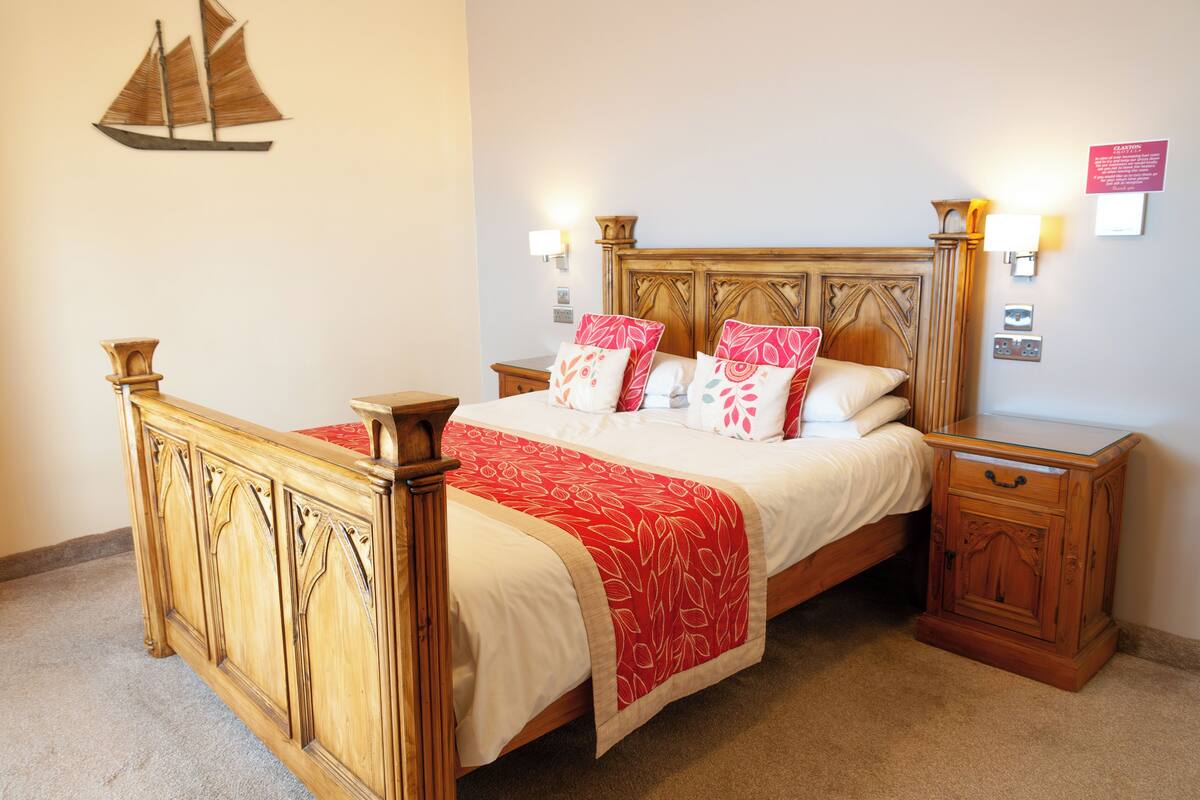 Un lit en bois avec une couvre-lit rouge et blanche, deux tables de chevet et une décoration murale représentant un navire.