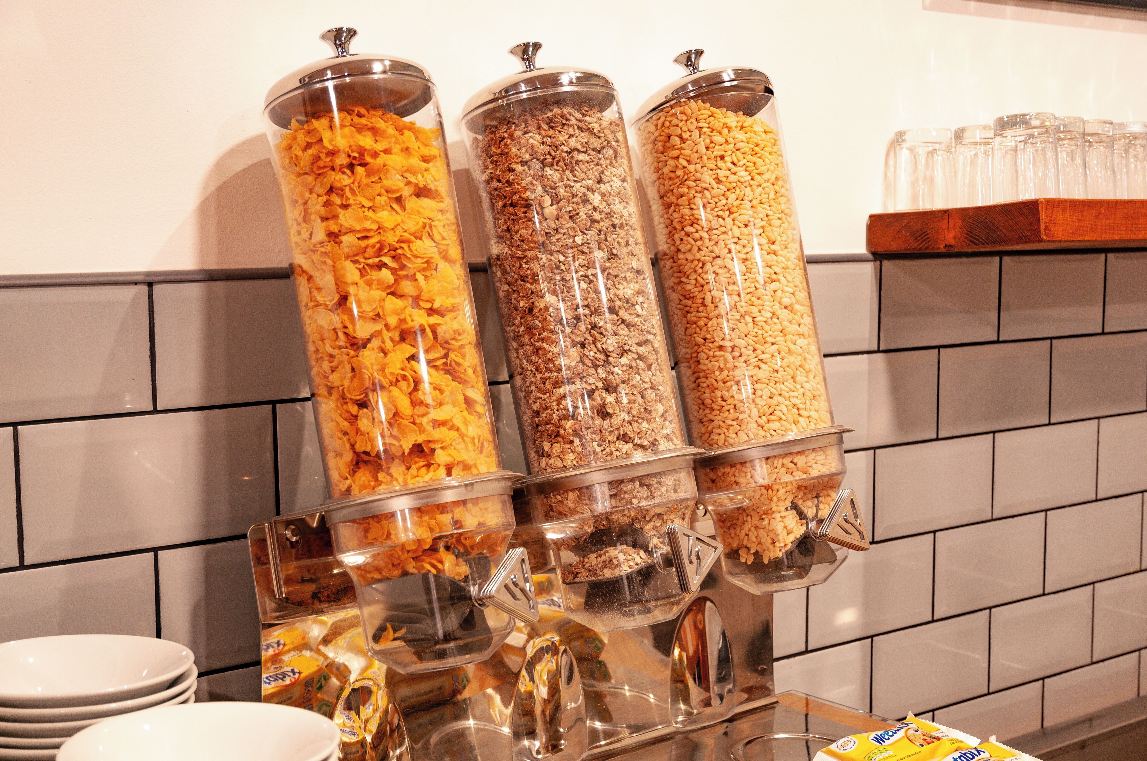A breakfast bar with three dispensers of cereal and granola.