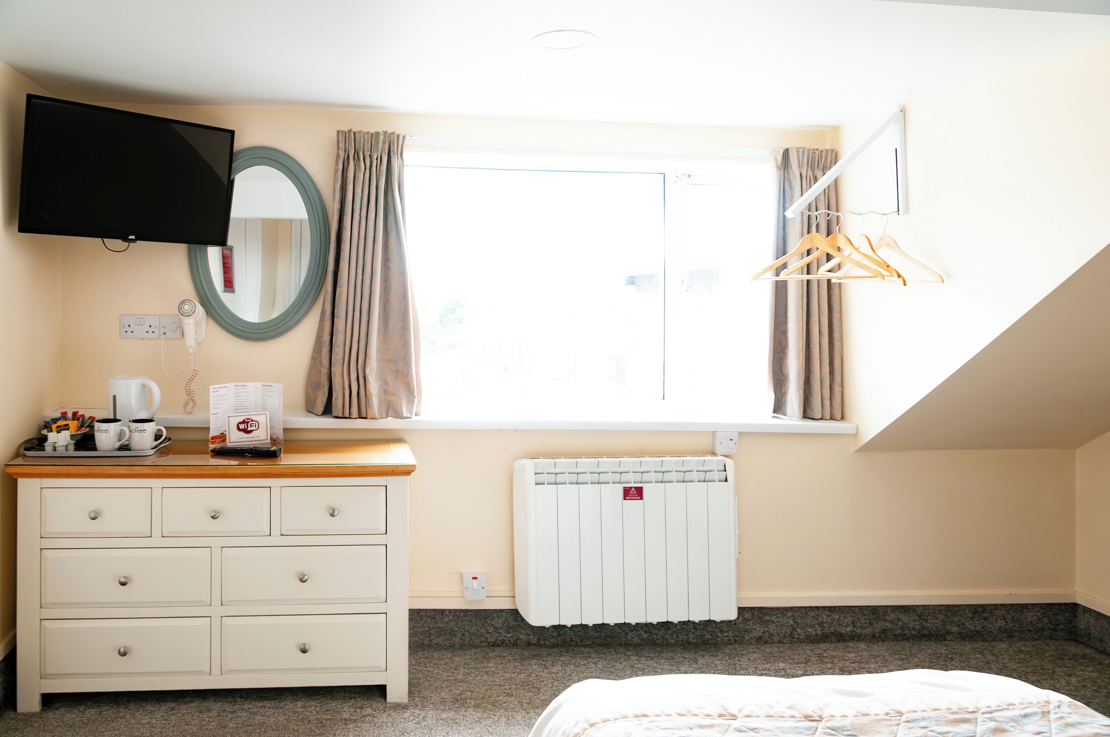 Quarto com cama, cômoda, televisão, janela com cortinas e radiador.