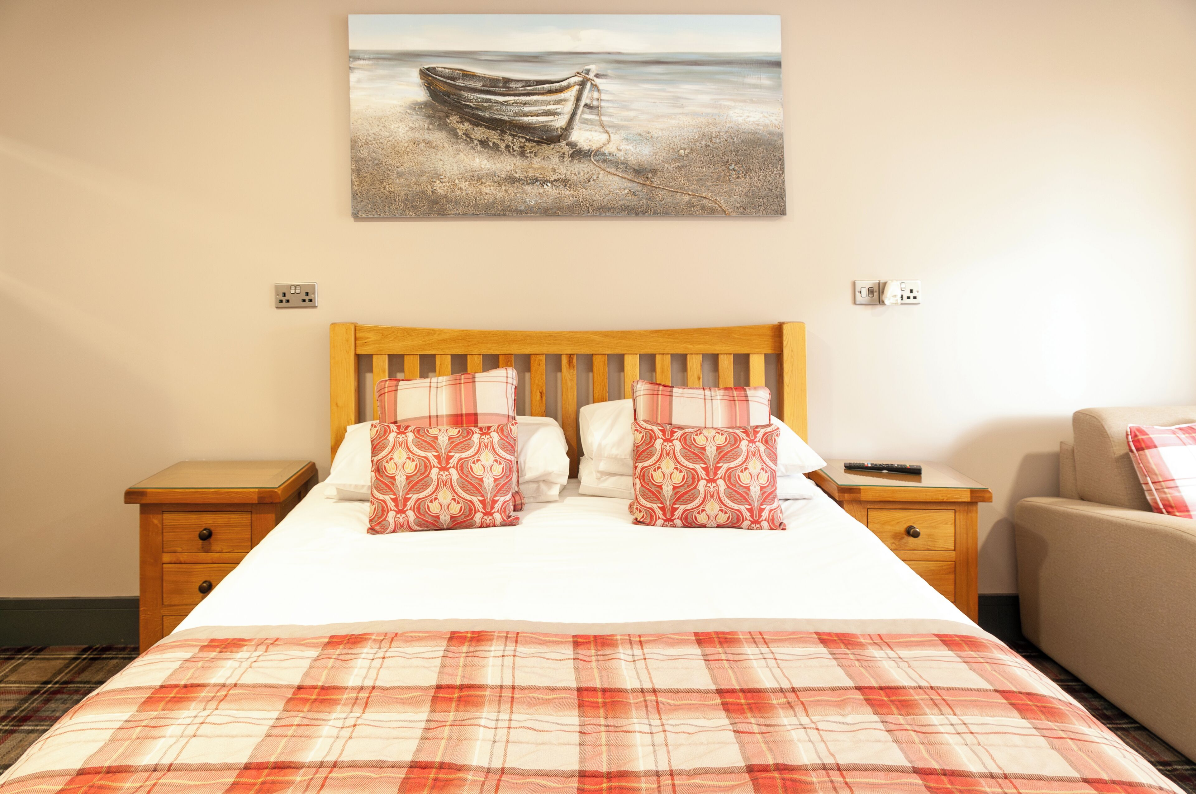 A bedroom with a wooden bed, two nightstands, a chair, and a painting of a boat on the wall.