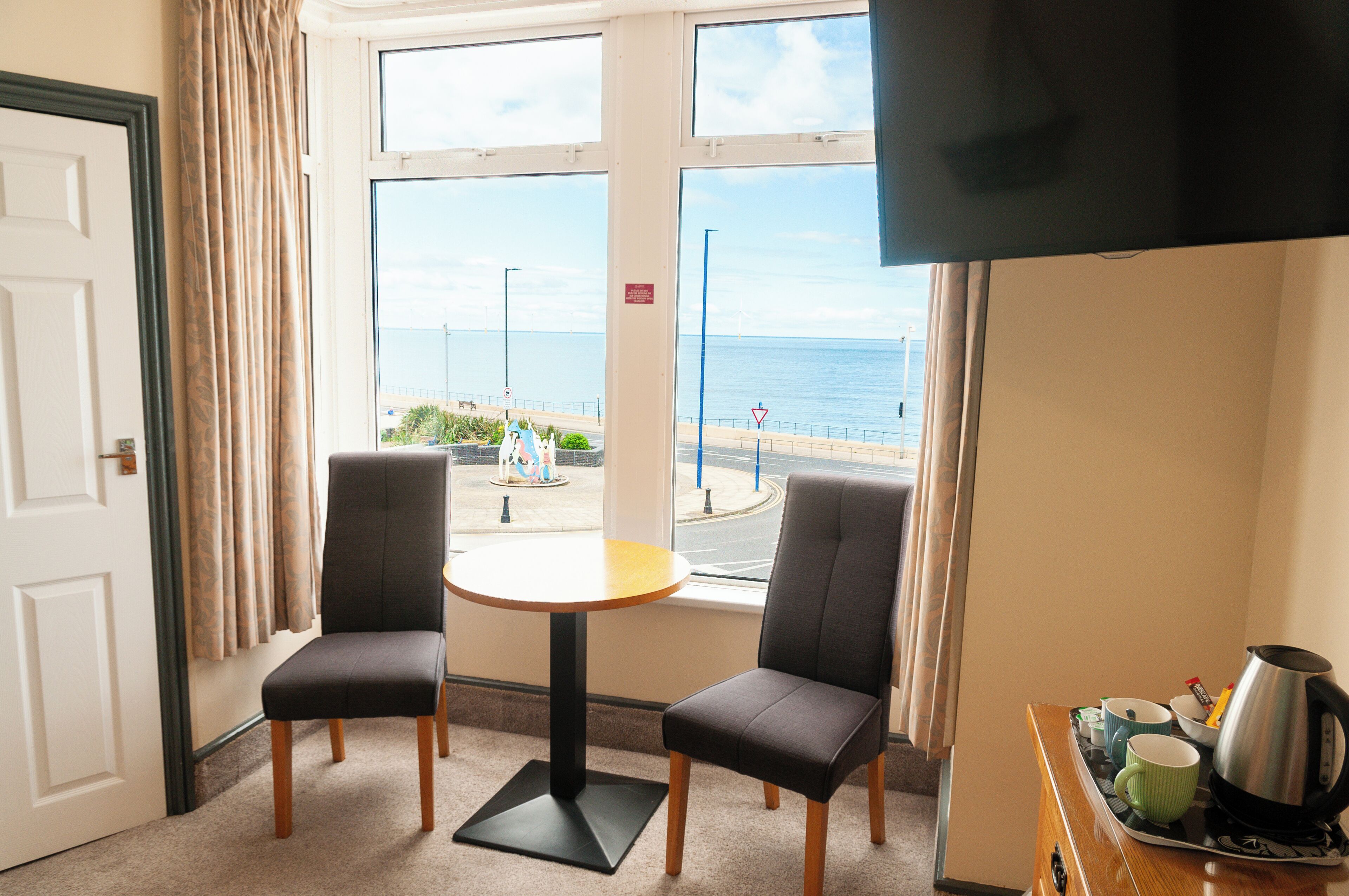 A room with two chairs, a small table, a TV, and a view of the sea.