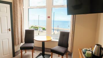 A room with two chairs, a small table, a TV, and a view of the sea.