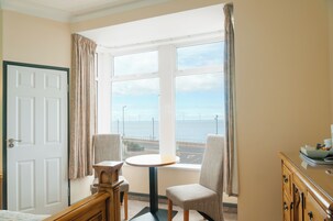 Una habitación con un ventanal grande que ofrece vistas al mar y a aerogeneradores, una mesa redonda, dos sillas, un armario de madera y una puerta.