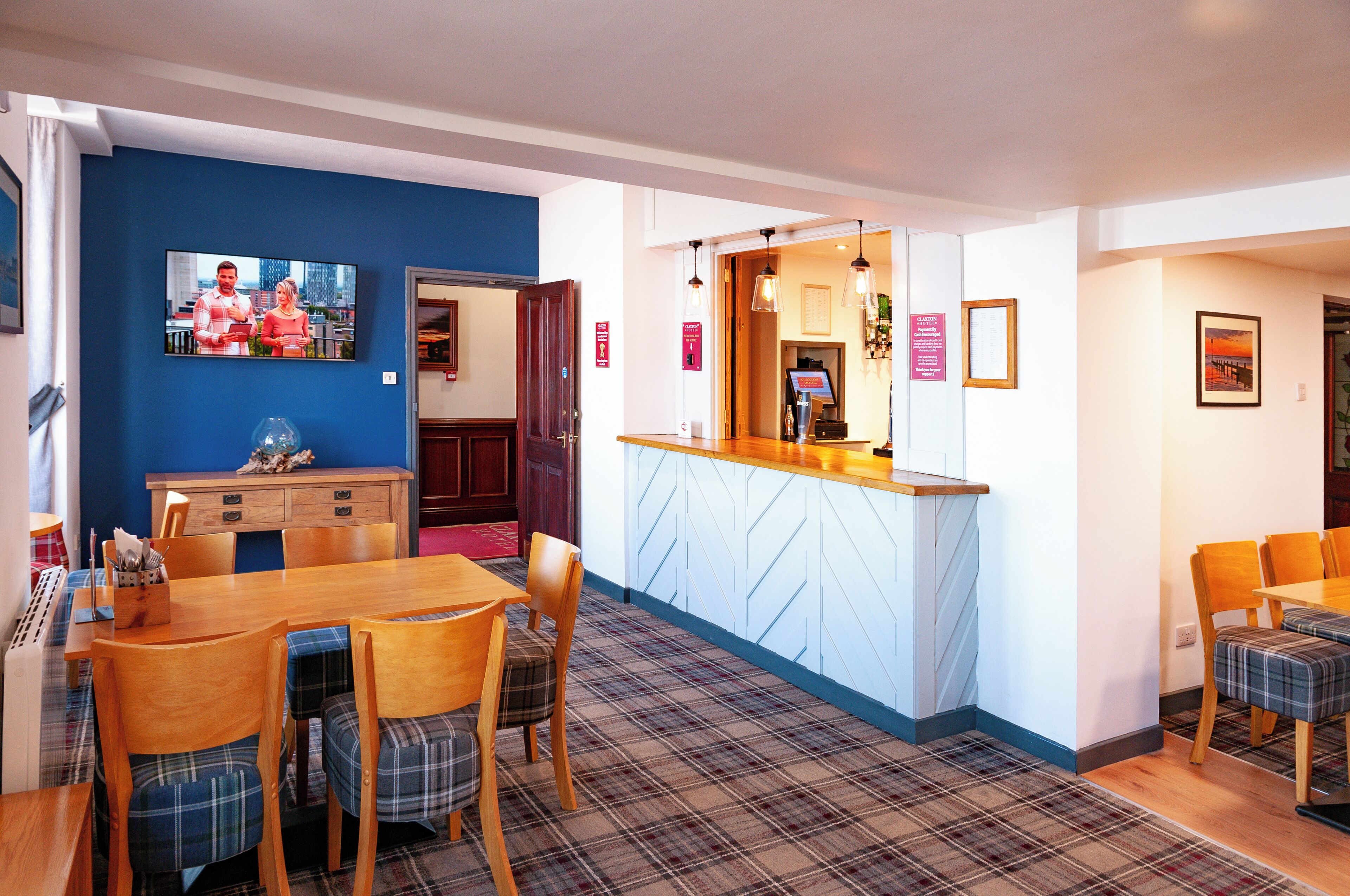 A dining area with a wooden table and chairs, a bar area with a counter, and a television mounted on the wall.