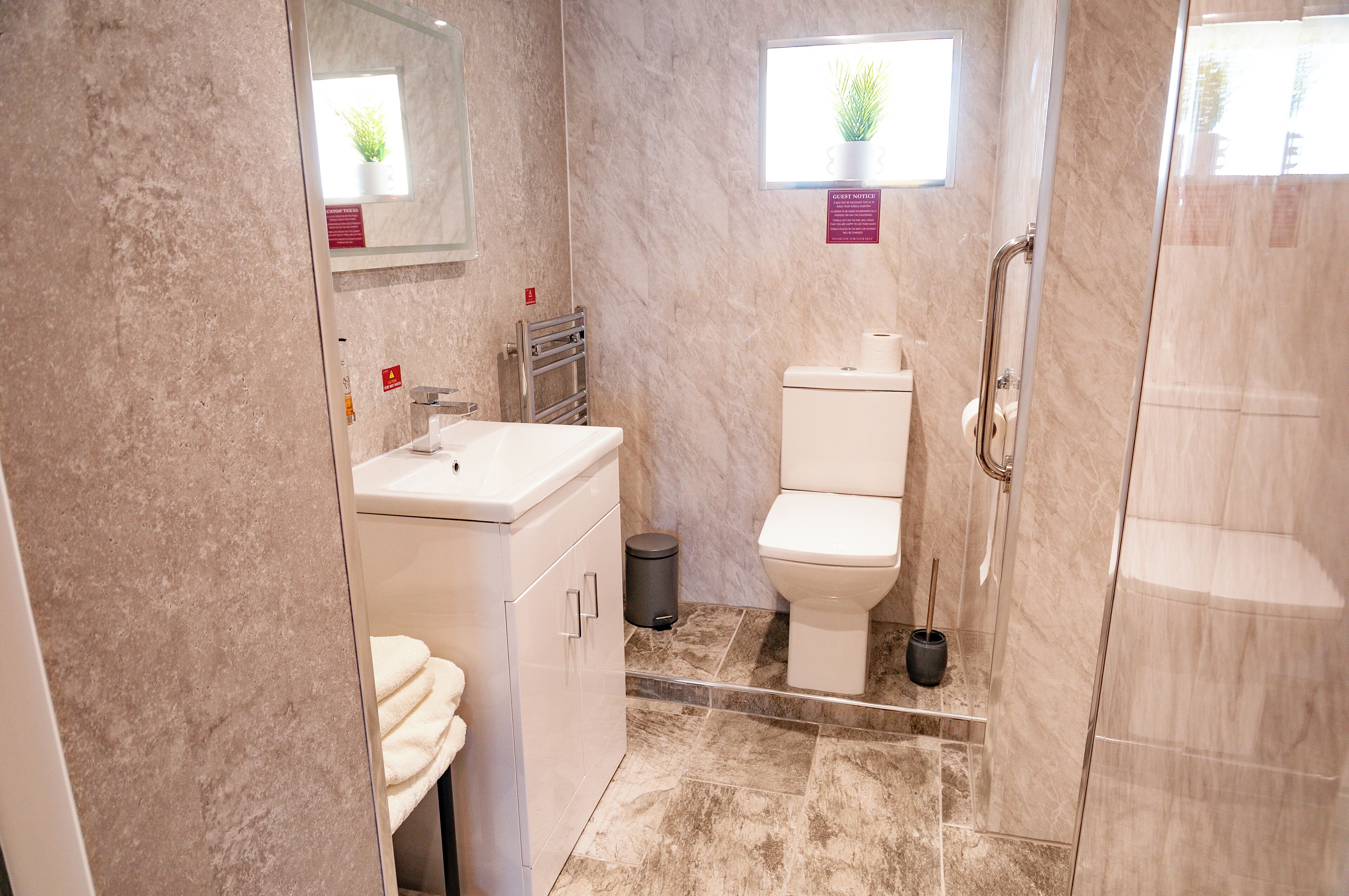Un baño moderno con piso de mármol, lavamanos blanco, inodoro y cabina de ducha de vidrio.