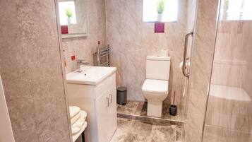 Un baño moderno con piso de mármol, lavamanos blanco, inodoro y cabina de ducha de vidrio.