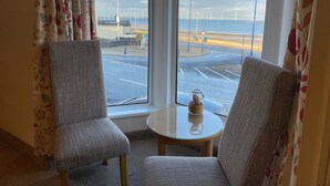 A room with two chairs facing a window overlooking a road and wind turbines.
