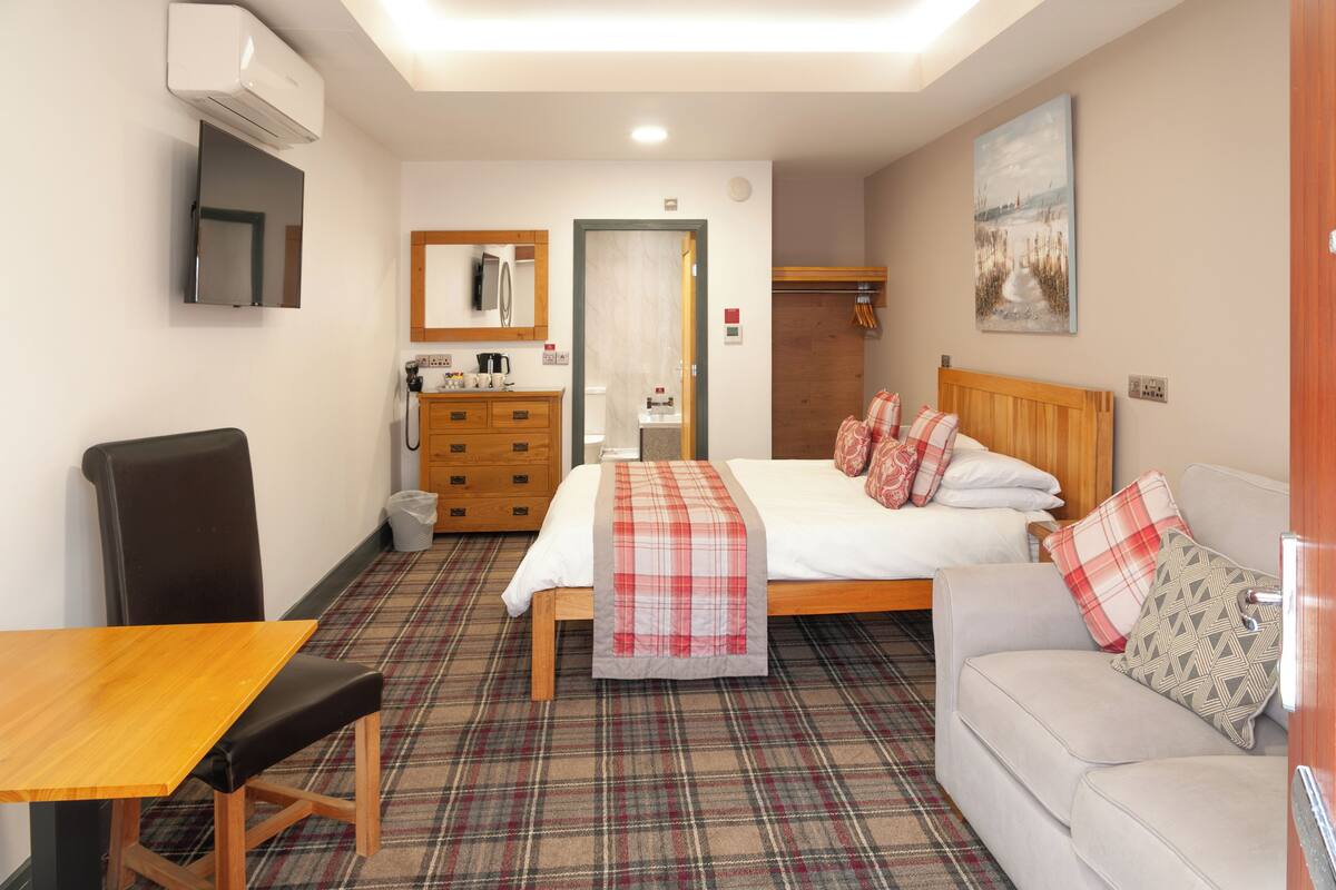 Une chambre d’hôtel comprenant un lit, un canapé, une table à manger, une chaise, un téléviseur, un miroir, une commode et un tableau accroché au mur.